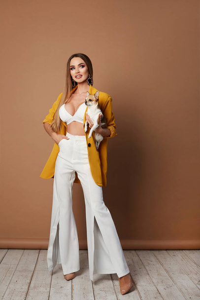 Longlegged young woman, with sexy perfect body and full lips, in yellow jacket and sexy lingerie sitting with cute dog chihuahua. Fashionable busty blonde model girl with long sexy legs in sexy outfit - Fotografie, Obrázek