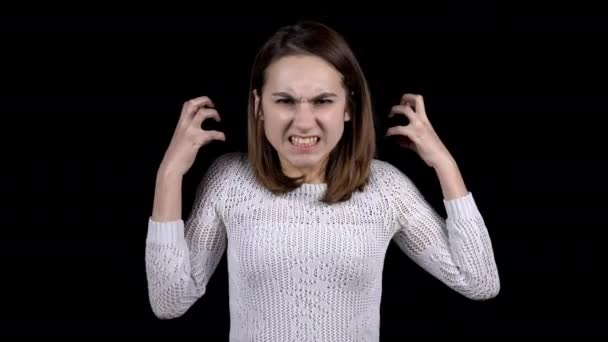 De jonge vrouw toont emoties van woede op zijn gezicht. Meisje grijnst tanden en fronst wenkbrauwen op een zwarte achtergrond. - Video