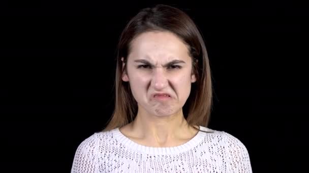 Een jonge vrouw toont walgelijke emoties op haar gezicht. vrouw contorts haar gezicht van gruwel op een zwart achtergrond closeup. - Video
