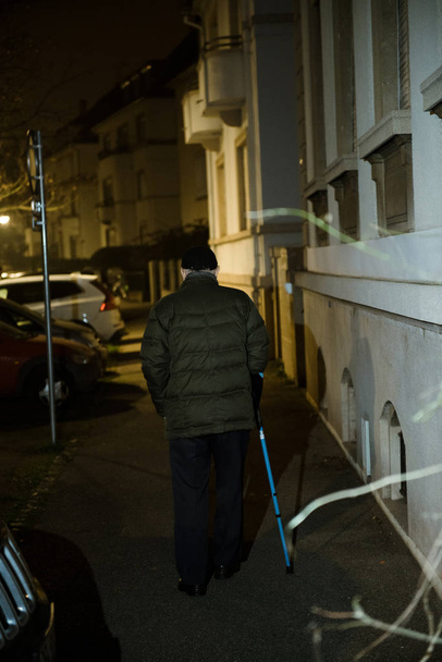 Προοπτική σκηνή του δρόμου με σιλουέτα του ηλικιωμένου ανθρώπου με τα πόδια στο γαλλικό δρόμο τη νύχτα χρησιμοποιώντας το περπάτημα ραβδί διατήρηση της ισορροπίας με τηλεσκοπικό αλουμίνιο ζαχαροκάλαμο Ιατρική βοήθεια και αποκατάσταση - Φωτογραφία, εικόνα