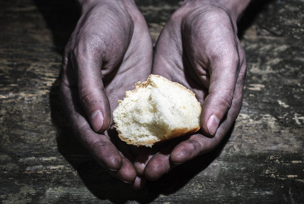 Lavorare le mani sporche di un uomo che tiene una crosta di pane. Implorando una mano di speranza. Dare speranza. Il concetto di elemosina e carità
 - Foto, immagini