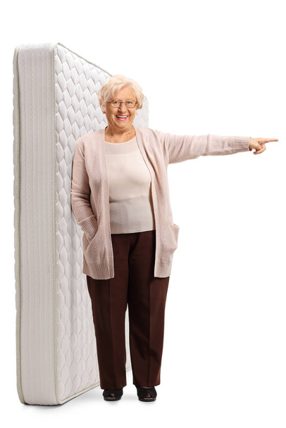 Elderly lady leaning on a bed mattres adn pointing to one side - Photo, Image