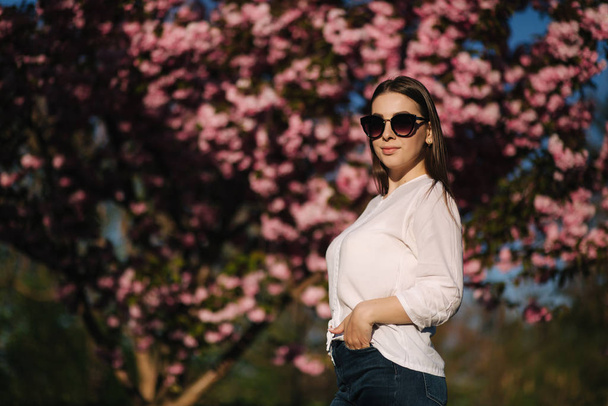 Attractive woman in white shirt in the park. Background of pink tree - Photo, Image