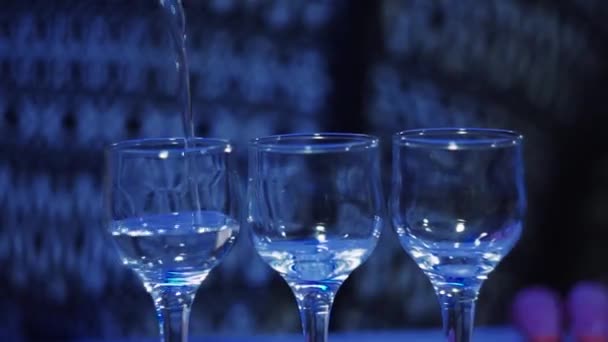 close-up of three glasses in a club bartender pours vodka from a bottle - Felvétel, videó