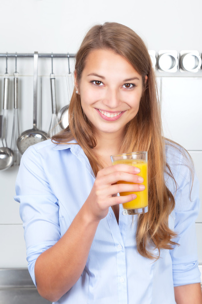 Laughing woman in the kitchen drinking orange juice - Фото, изображение