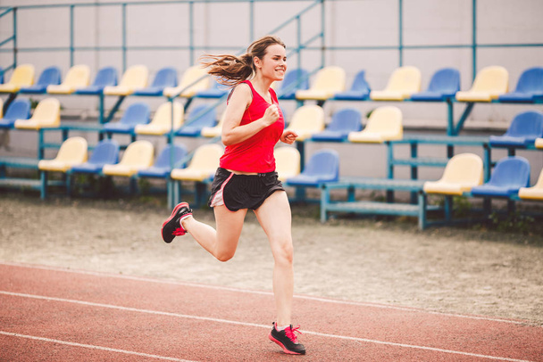 Woman Running At Stadium. Young woman running during on stadium track. Goal achievement concept. Fitness Jogging Workout on ballpark. Wellness theme. Sporty training cardio for weight loss success - Photo, Image