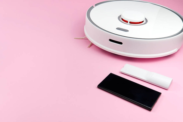 blanc Aspirateur robotique, smartphone et télécommande isolé sur fond rose avec espace de copie
 - Photo, image