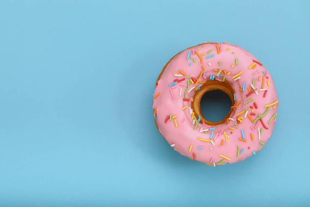 Pink donut on a blue background, top view, concept of desserts, pink color on blue. Copy space, blue background. - Foto, Imagen