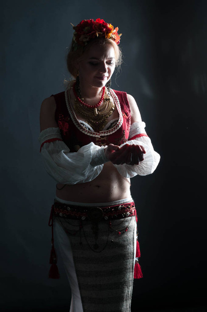 Низкий портрет с задним светом женщины в традиционном народном славянском костюме для танцев, держась за руки возле груди, изолированной на черном
 - Фото, изображение