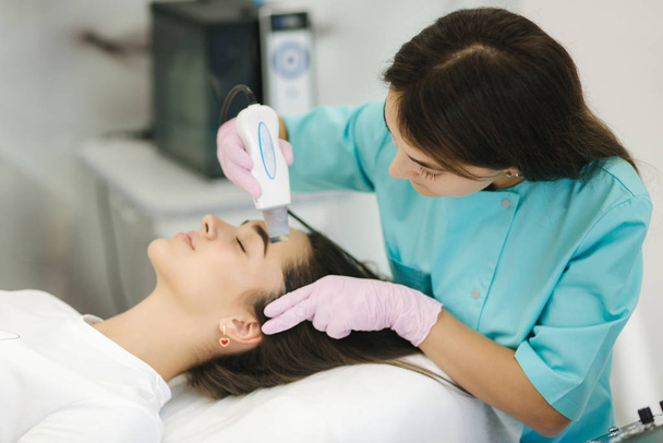 Kobieta w kosmetycznej klinice uzdrowiskowej ma kosmetologię sprzętu do twarzy. Kobieta robi zabiegi kosmetyczne - Zdjęcie, obraz