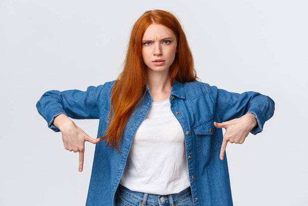 Mad and disturbed, questioned redhead woman waiting answer on question, pointing fingers down, frowning angry and distressed, cat made mess while she was at work, scolding over white background - Photo, Image