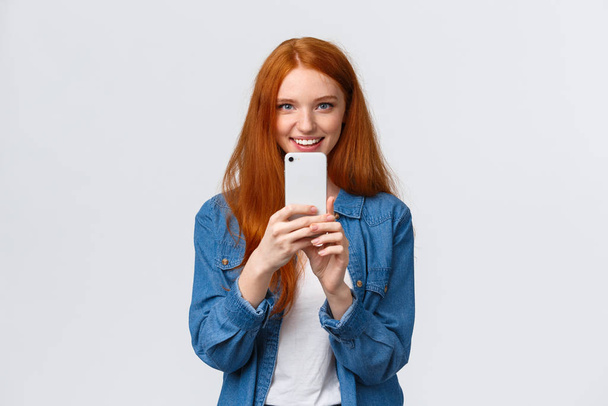Friendship, togetherness and modern lifestyle concept. Cute redhead girl searching perfect angle, taking shot of friend on smartphone, phogotaphing, shooting something interesting - Фото, зображення