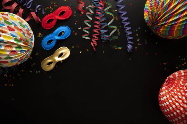 Karnevalové objekty na černém pozadí. Svitky, masky, papírová kostra, konfety, papírové balónky a mnoho dalších karnevalových předmětů - Fotografie, Obrázek