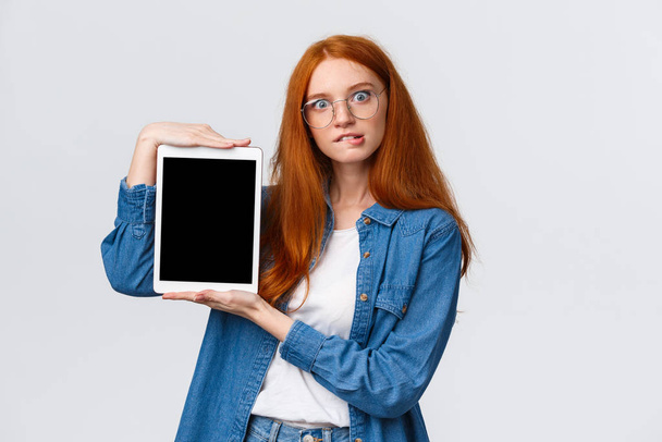 Cant resist temptation, add to cart now. Tempting and curious good-looking excited redhead woman in glasses, biting lip desire buy something online, showing digital tablet screen, white background - Фото, изображение