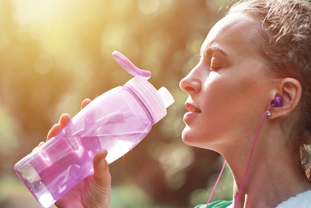 Fitness woman drinking water after running training in summer park - Photo, Image