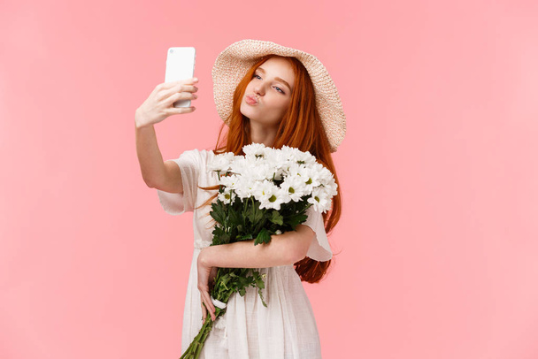 Typerä ja söpö, naisellinen tyttö bloggaaja ottaa selfie kukkakimppu poikaystävä toi, tilalla älypuhelin taitto huulet ilman suudelma, poseeraa täydellinen aistillinen laukaus, seistä vaaleanpunainen tausta - Valokuva, kuva