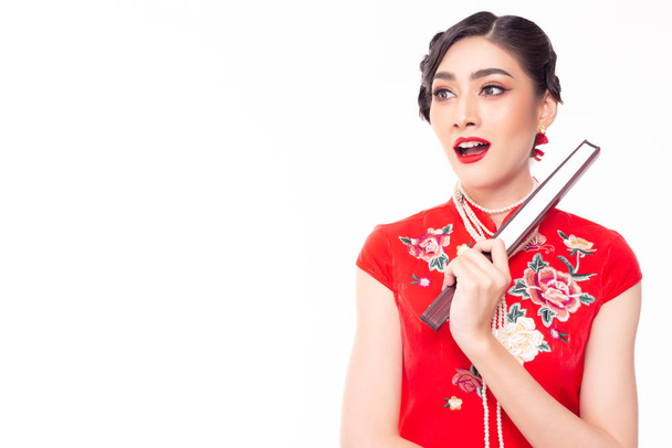 Jovem chinesa encantadora olha para o espaço de cópia. Atraente bela menina asiática vestir vestido chinês, segurando ventilador chinês no dia de Ano Novo Chinês. Ela fica surpresa, feliz quando olha para o produto
 - Foto, Imagem