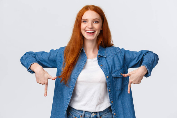 Must have, check this out. Waist-up portrait alluring, friendly redhead woman showing you good promo banner, review product, blogger indicate down, bottomg advertisement, white background - Photo, Image