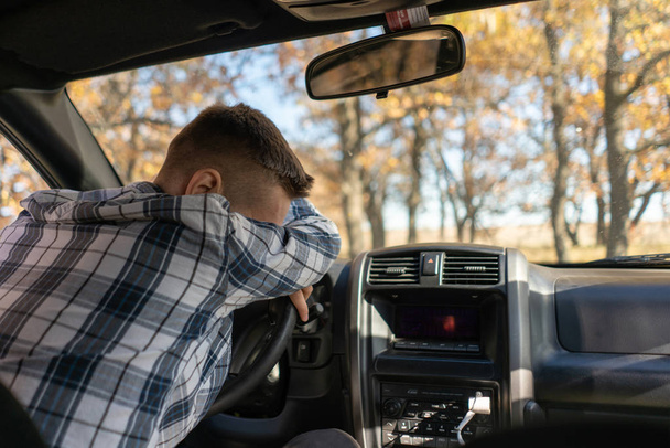 een jonge man die in de auto op de bestuurdersstoel slaapt en na een lange rit rust neemt - Foto, afbeelding