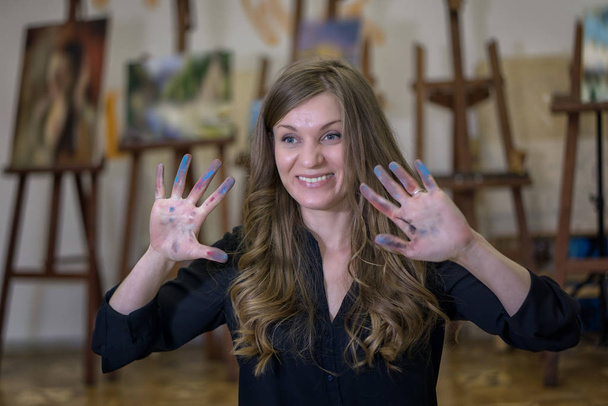 Artist in the art studio shows her hands stained with paints. - Zdjęcie, obraz