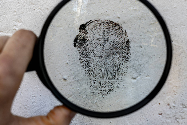 een misdaadonderzoek, een vergrootglas en de vingerafdruk op de oppervlaktestructuur - Foto, afbeelding