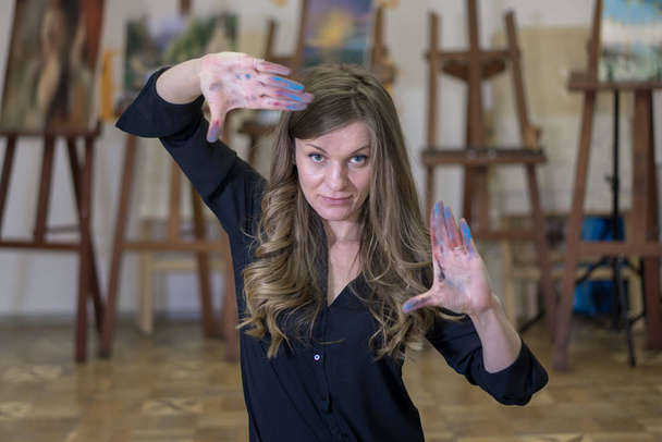 Художник в художественной студии показывает рамку из своих рук, окрашенных красками
. - Фото, изображение
