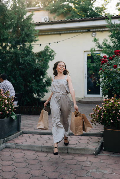 Photo of a joyful stylish girl with shopping bags walking down the street of the city - Zdjęcie, obraz