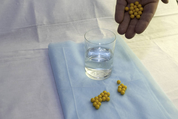 la mano del médico vierte pastillas en un vaso de agua sobre una sábana médica azul
 - Foto, imagen