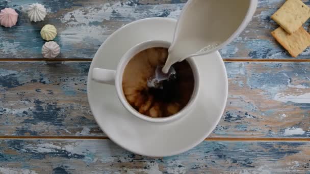 Hand adding milk to coffee in a cup on wooden table, top view - Filmati, video
