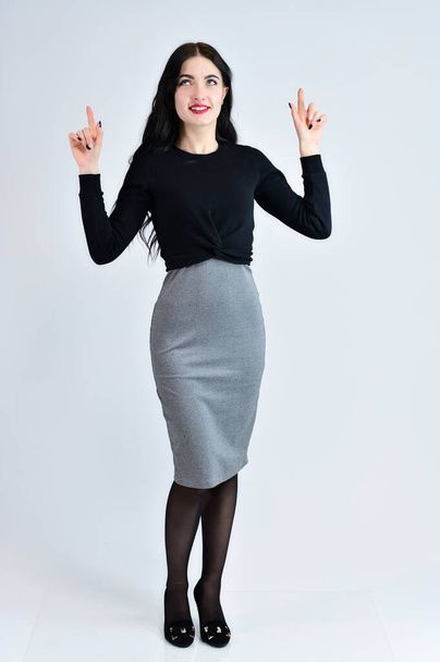Portrait of a pretty brunette girl with a smile with long hair with excellent makeup in a gray dress on a white background is standing straight. Concept of business female photo portrait. - Valokuva, kuva