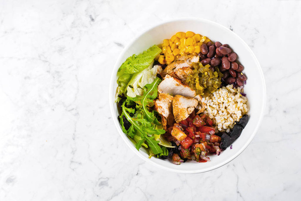 Mexican Lunch bowl on marble background. Salad bowl with corn, red beans, tomato with red onion, jalapenios, chicken breast. Top view, copy space - Photo, Image
