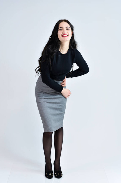 Concept of business female photo portrait. A brunette girl with a smile with long hair with excellent makeup in a gray dress on a white background stands right in different poses in full growth. - Photo, Image