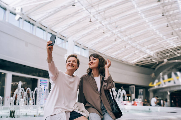 Two girls take a selfie in the mall, a fountain in the background - Fotografie, Obrázek