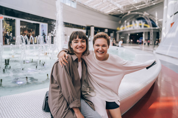 Two girls have fun in the mall, a fountain in the background - Foto, Bild
