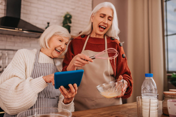 Grey-haired smiling lady in apron showing something on her smartphone - Foto, Imagem