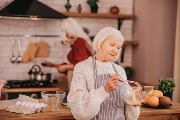 Grey-haired smiling lady in apron looking involved - Fotografie, Obrázek