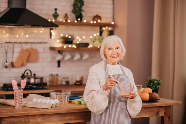 Grey-haired smiling lady standing near the table in the kitchen - Valokuva, kuva