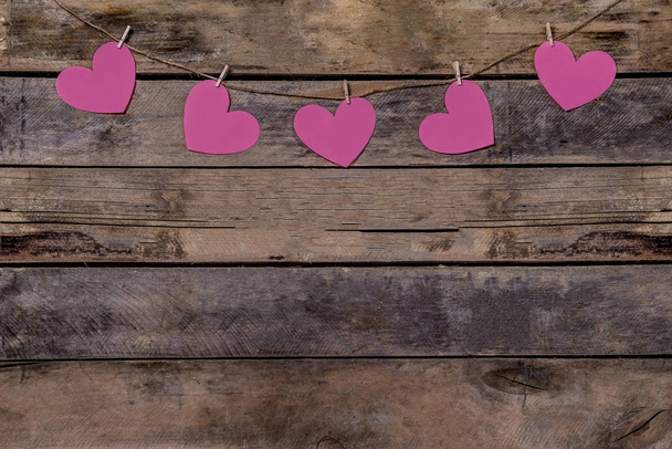 Old wooden background with a garland of pink hearts. Natural rope and clothespins. Concept of recognition of love, romantic relationships, Valentines day in grunge style. Copy space - Photo, image