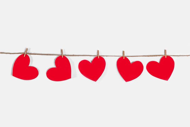Garland of red hearts on a white isolated background. Natural rope and clothespins. The concept of recognition in love, romantic relationships, Valentines Day. Copy space - Фото, изображение