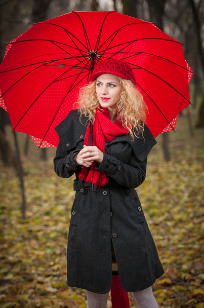 Attractive young woman in a autumn fashion shoot. Beautiful fashionable young girl with red umbrella, red cap and red scarf in the park. - Fotó, kép
