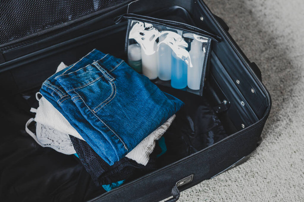 travel essentials and packing light for a holiday concept, luggage with pile of clothes next to transparent liquid bag for airport security screening compliance - Photo, Image