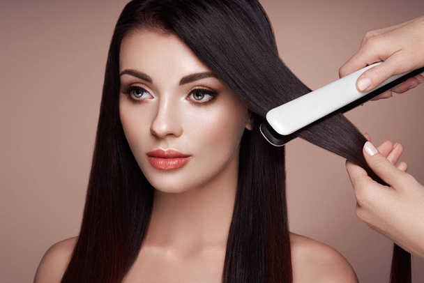 Hairdresser straightening long hair with hair irons - Foto, imagen