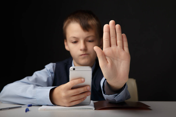 Social cyberbullying concept. Serious kid showing stop sign holding phone isolated. - Photo, Image