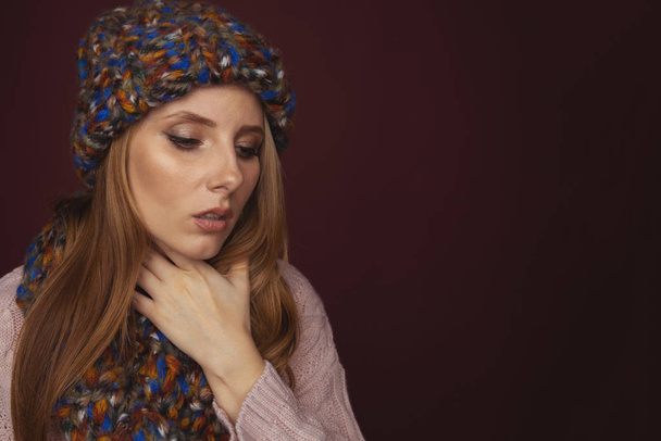 Sore throat concept. Closeup view of woman in sweater and hat with scarf holding her neck in pain. - Photo, Image