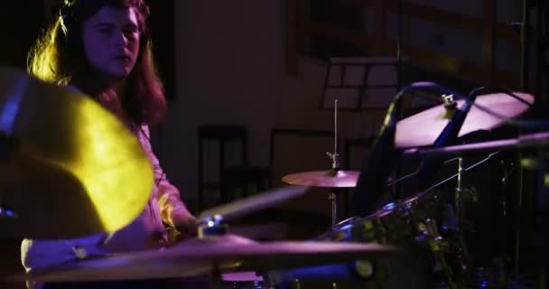 Side view of a Caucasian man with long dark hair wearing headphones and playing a drum kit during a session at a recording studio. Musicians working on producing a song - Кадры, видео