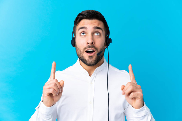 Telemarketer man working with a headset over isolated blue background pointing with the index finger a great idea - Photo, image