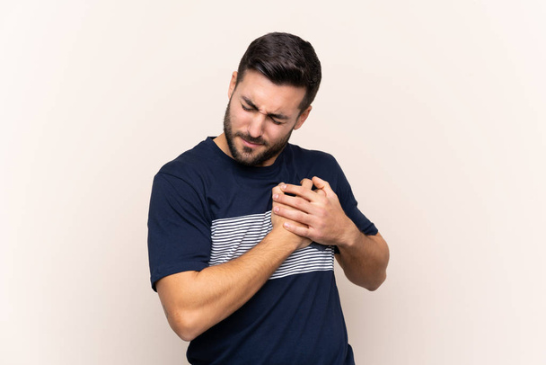 Young handsome man with beard over isolated background having a pain in the heart - Photo, image