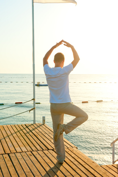 mens staande op een pier op één been en houdt het evenwicht - Foto, afbeelding