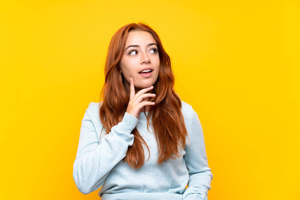 Teenager redhead girl over isolated yellow background thinking an idea while looking up - Photo, Image