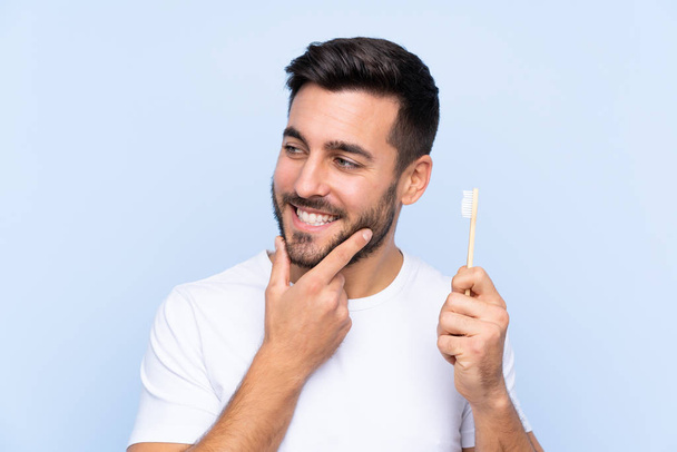 junger gutaussehender Mann mit Bart beim Zähneputzen über isoliert aussehender Seite - Foto, Bild
